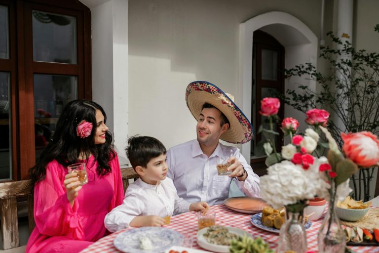 A joyful family gathering featuring a man in a sombrero, surrounded by flowers and food at a festive table.
