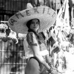 Black and white portrait of a woman in traditional Mexican attire with sombrero, outdoors.