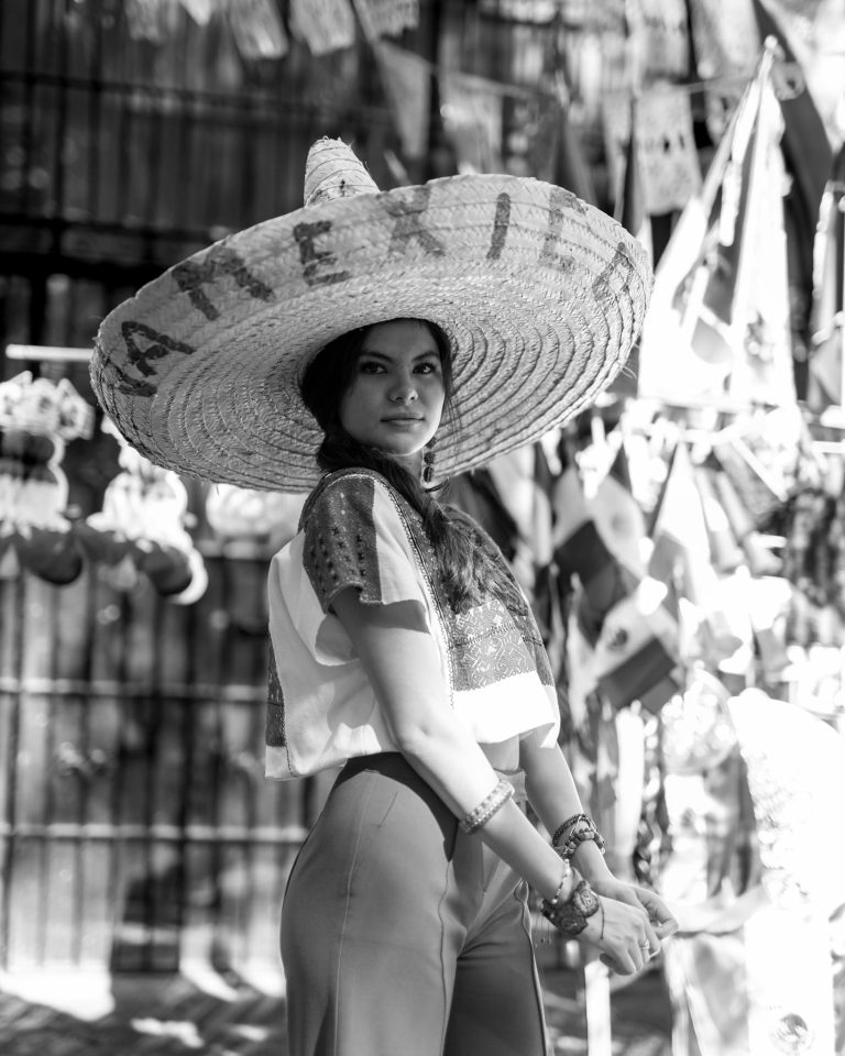Black and white portrait of a woman in traditional Mexican attire with sombrero, outdoors.