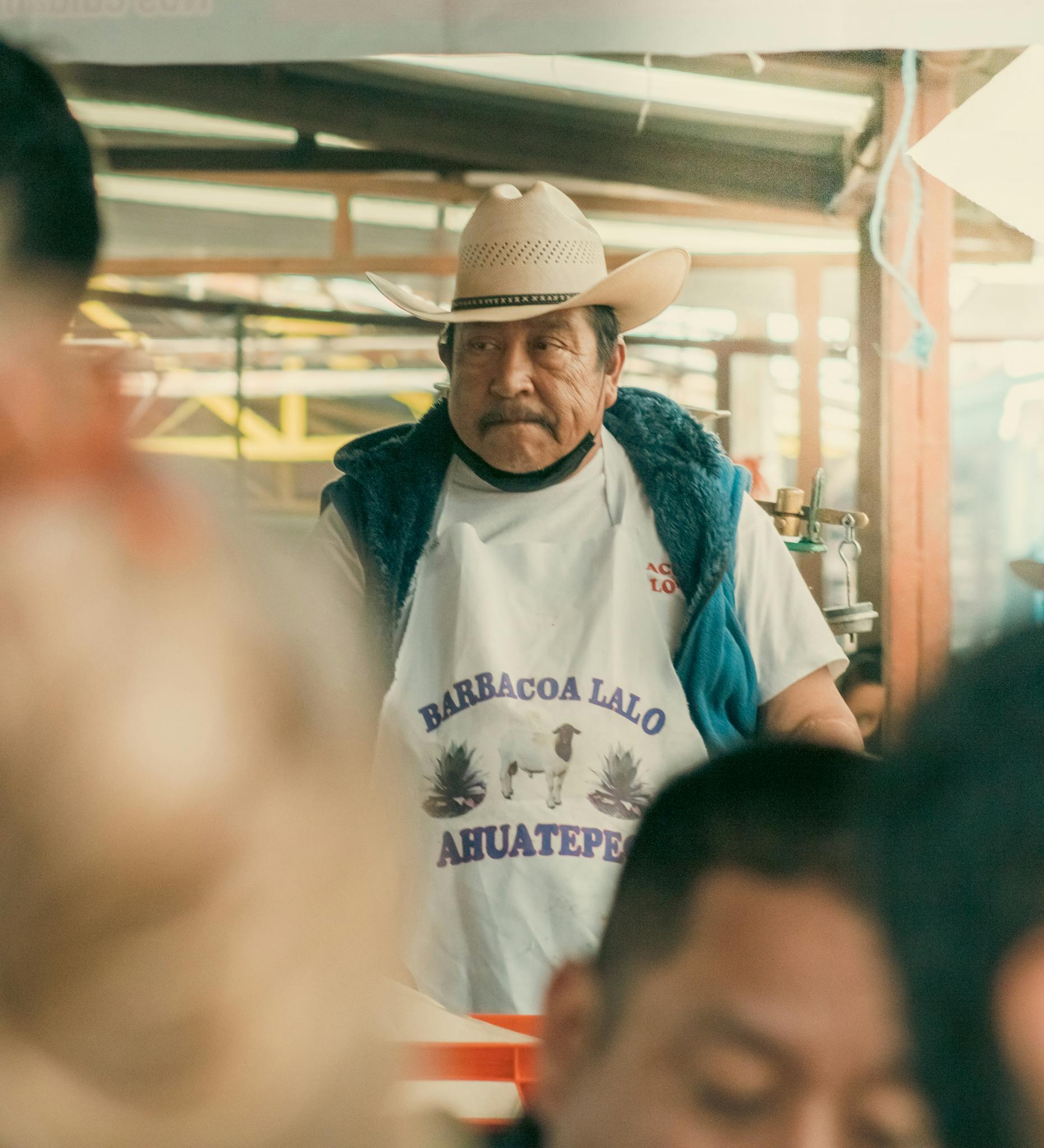 Elderly man wearing cowboy hat serves at a Mexican barbecue stall.